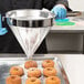 A person in a blue uniform using a Vollrath fine china cap strainer to sprinkle sugar on a doughnut.