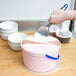 A person using a Vollrath blue aluminum ice cream spade to scoop ice cream into a white bowl.