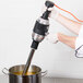 A person using a KitchenAid 400 Series immersion blender to mix liquid in a metal container.