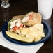 A Carlisle Dallas Ware cafe blue melamine plate with a sandwich, pickle, and potato chips.