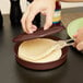 A person using a Carlisle Lennox brown tortilla server to put tortillas into a pan.