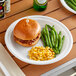 A Dart Famous Service white plastic plate with a sandwich and corn on the cob on a table.