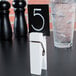 An American Metalcraft white clothespin card holder with a number on a table.