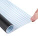 A hand holding a roll of American Metalcraft chalkboard paper with a grid pattern.