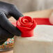 A hand in a black glove holding a red rose made of Satin Ice red gum paste on a white cake.