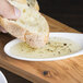 A person holding a piece of bread dipping it into a small white Arcoroc porcelain dish filled with oil.