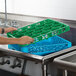 A hand using a green Carlisle glass rack extender in a metal sink.