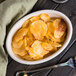 An ivory oval baker dish filled with potato chips on a table with a fork and knife.