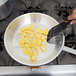 A person using a spatula to stir eggs in a Vollrath Arkadia aluminum fry pan.