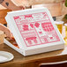A white, clay-coated, customizable pizza box with red printed graphics being opened on a wooden table.