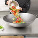 A chef using a Town hand hammered Cantonese wok to prepare a bowl of vegetables.