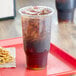 A red tray with a plastic cup of brown liquid with ice and a napkin on it.