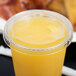 A clear plastic lid with a straw slot on a plastic cup of yellow liquid.