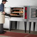 A man in an apron baking bread in a Vulcan gas convection oven.