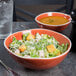 An Arcoroc orange porcelain bowl filled with salad on a table.