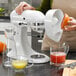 A woman uses a KitchenAid citrus juicer attachment to juice oranges into a glass pitcher.