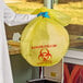 A person in a lab coat holding a yellow infectious linen and medical waste bag with a biohazard symbol.