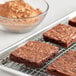 A brownie on a cooling rack with a bowl of HERSHEY'S cocoa powder.