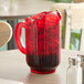 A Vollrath Traex Tuffex ruby red pitcher filled with red liquid on a table.