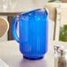 A Vollrath Traex Tuffex cobalt blue plastic pitcher on a table with ice and liquid.