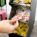 A hand taking a packet from a Vollrath condiment holder on a counter.