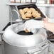A woman using a Hobart countertop potato peeler to prepare a tray of potatoes.