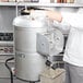 A person in a white coat and gloves using a Hobart countertop potato peeler.