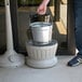 A man holding a silver metal pail with a black metal cylinder inside.