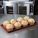 A burgundy MFG Fiberglass Display Tray of muffins on a counter.