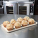 A beige MFG Tray supreme display tray holding muffins on a counter.