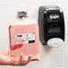 A hand holding a clear plastic bottle of GOJO® Luxury Cranberry Foaming Hand Soap with pink liquid inside.