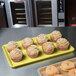 A MFG Tray yellow fiberglass display tray holding muffins on a counter.