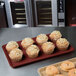 A burgundy MFG fiberglass display tray with muffins and a donut on a counter.