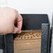 A hand picking up a Vollrath vertical coffee sleeve dispenser from a black cardboard box.