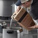 A man pouring 35 lb. High Performance Canola Fry Oil from a box into a fryer.