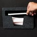 A hand holding a straw in a black Vollrath straw dispenser.