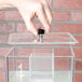 A hand pressing a black button on a clear Cal-Mil beverage dispenser lid.