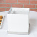 A white table with a Cal-Mil Luxe beverage dispenser base on top of a white box with a lid.
