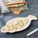 A TreeVive by EcoChoice palm leaf bowl filled with a sandwich and salad on a table.
