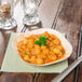 A TreeVive by EcoChoice square palm leaf plate with chickpeas and parsley on a wood surface.