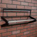 A Bulman black metal paper dispenser rack on a brick wall.