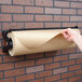 A person using a Bulman black paper dispenser to cut brown paper on a wall.