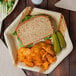 A sandwich with chips and a pickle on an EcoChoice palm leaf plate on a table.