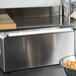 A metal Edlund film dispenser blade in a stainless steel box on a counter with a paper holder.