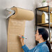 A woman using a Bulman paper dispenser to write on a paper roll on a table.