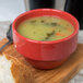 A red Libbey porcelain bouillon bowl filled with soup on a wooden surface.