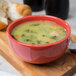 A Libbey porcelain bouillon bowl filled with soup on a wood surface.