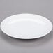 A Libbey Aluma White porcelain coupe plate with a rim on a gray surface.