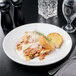 A white Libbey porcelain pasta bowl with a plate of food on a table.