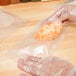 A person in plastic gloves using an ARY VacMaster plastic bag to vacuum package a piece of food.